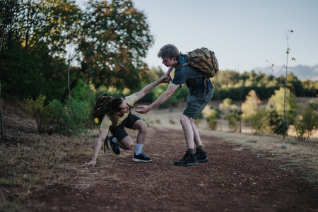 Two hikers help each other on a dirt trail during an outdoor forest hike