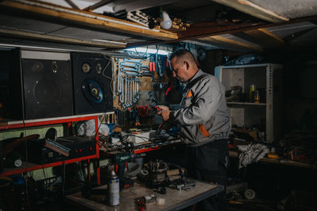 A mechanic works in a cluttered workshop repairing electrical components with tools and equipmentの写真素材