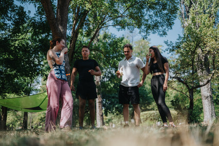 Friends enjoy a sunny park gathering with snacks and casual conversation among treesの写真素材