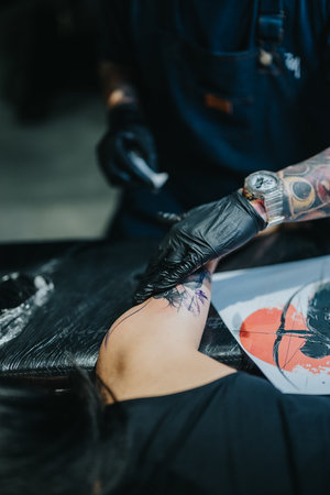 Tattoo artist in gloves applying a tattoo on a clients forearm during a studio sessionの写真素材