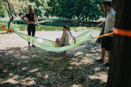 Friends in a park relax in a light hammock between trees on a sunny outdoor dayの写真素材