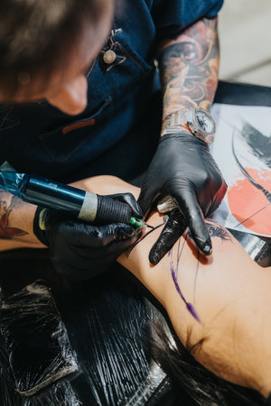 Tattoo artist in gloves working on a clients leg with a tattoo machine and inkの写真素材