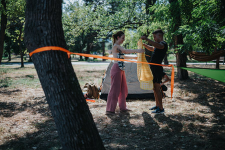 Couple setting up a hammock and camping gear in a sunny park for outdoor leisureの写真素材