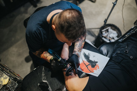 Tattoo artist at work tattooing a design on a clients leg in a studio.の写真素材