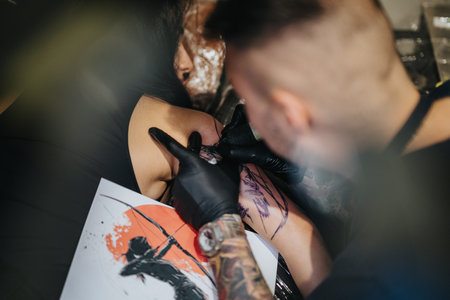 Tattoo artist works on a clients arm with stencil during a focused tattoo session