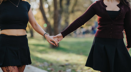 Two women hold hands in a park, expressing friendship, unity, and carefree outdoor moments