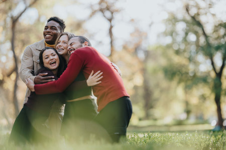 Diverse group of friends and family sharing a joyful hug in a sunny parkの写真素材
