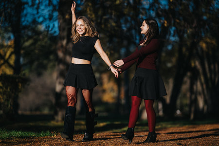 Two friends dance hand in hand in a sunny autumn park, expressing joy and friendshipの写真素材