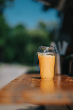 Orange smoothie in plastic cup on wooden table with blurred background outdoorsの写真素材