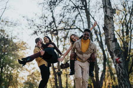 Happy friends enjoy a playful park outing as a group carry their friend laughingの写真素材