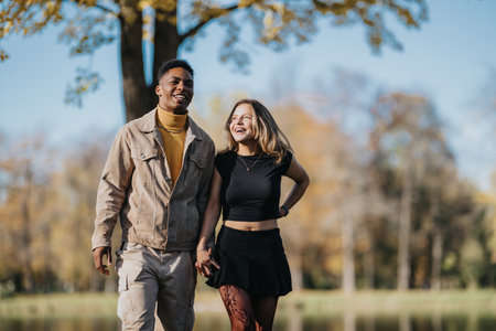Two friends walk hand in hand through autumn park, smiling and enjoying a sunny day.