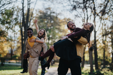 Joyful friends carry a woman in a park during fall afternoon, celebrating friendship and funの写真素材