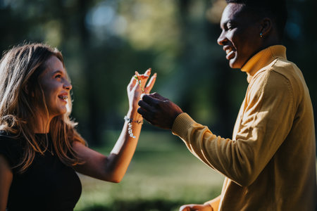 Happy couple outdoors in a park sharing a ring, smiling and enjoying a sunny moment togetherの写真素材