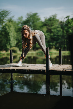 Woman stretching on wooden pier surrounded by scenic green forest and waterの写真素材