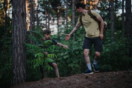 Two hikers in a forest helping each other navigate a steep trail during a hike