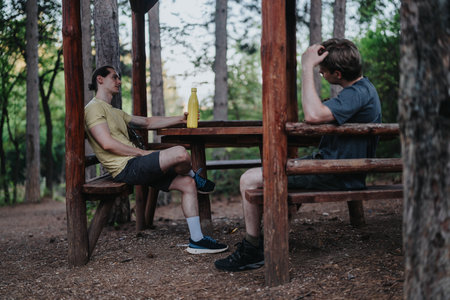 Two friends chat at a wooden picnic table in a forest parkの写真素材