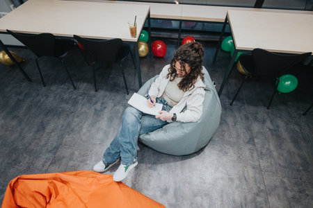 Student at the collaboration center writing in a cozy bean bag while others sit at desks with balloons aroundの写真素材