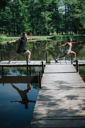 Two diverse individuals practicing yoga on a wooden dock over a calm lakeの写真素材