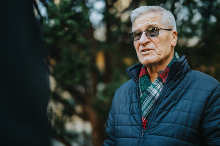Elderly man in a warm blue jacket outdoors, sharing a thoughtful conversation and everyday moment