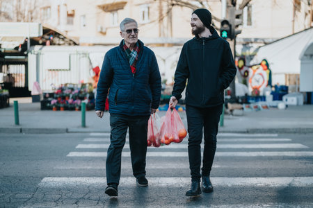 Two men cross a busy city street at a crosswalk, carrying pink shopping bags on a chilly dayの写真素材
