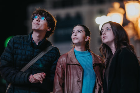 Three teenage friends stand in the city at night, looking up with curiosity and wonder