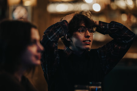 Young person with glasses in a warm, dim city night, hands in hair, captured with friends and...