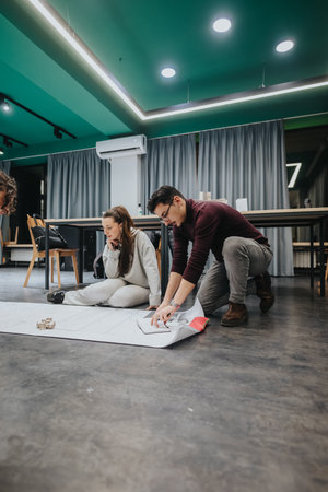 Two colleagues collaborate on a floor plan at a modern collaboration center, studying blueprints...