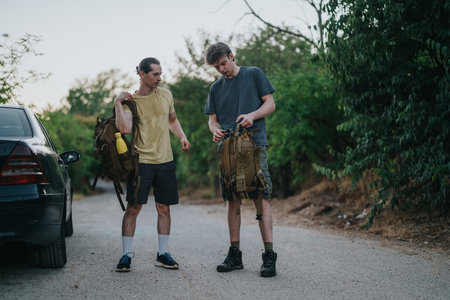 Two friends with backpacks preparing for a hike on a rural road near a parked car