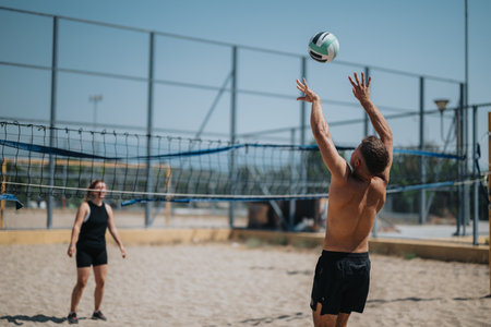 Two beach volleyball players compete on a sunny sand court as one leaps to spike the ball over the netの写真素材