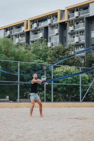 Man plays beach volleyball on sand court with urban apartment buildings in the backgroundの写真素材