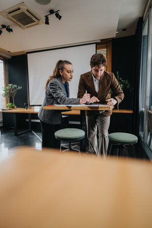 Two business coworkers review documents at a standing table in a modern, professional officeの写真素材