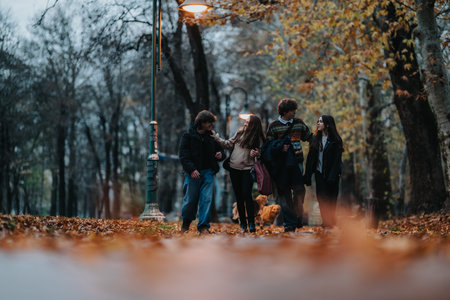 Teenage friends walking together in autumn park under street lamps, enjoying fall eveningの写真素材