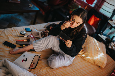Young woman applies makeup on bed at home with cosmetics and a cute tote bag in a cozy bedroomの写真素材