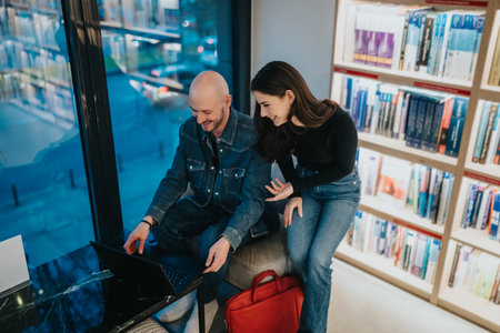 Couple works on a laptop in a library setting, smiling and sharing ideasの写真素材