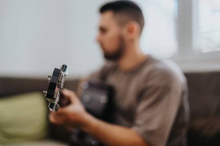 Man with acoustic guitar relaxing at home, focused on playing in a casual settingの写真素材