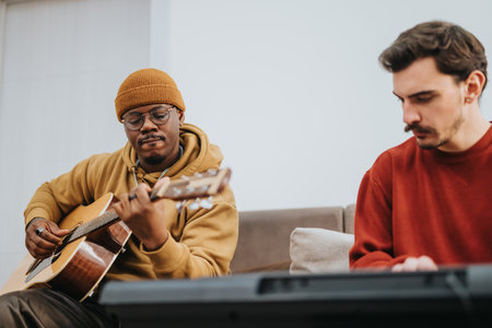 Two men play guitar and keyboard in a cozy living room settingの写真素材