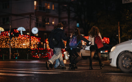 Teenagers crossing a city street at night among festive lights with backpacksの写真素材