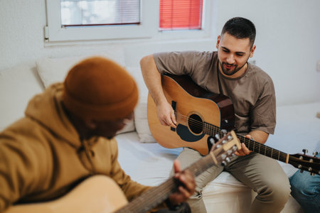 Two friends play acoustic guitar together in a cozy living room setting and share musicの写真素材