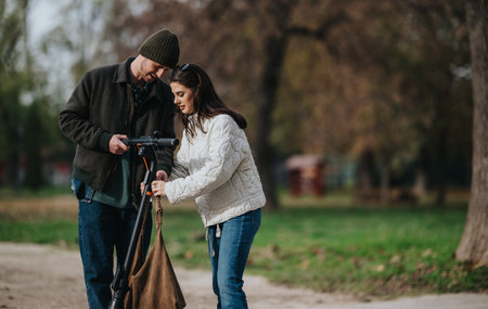 Couple adjusts a camera together in a park during autumn, enjoying a casual outdoor momentの写真素材