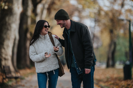 Happy couple walking and laughing in autumn park, wearing jackets and sunglassesの写真素材