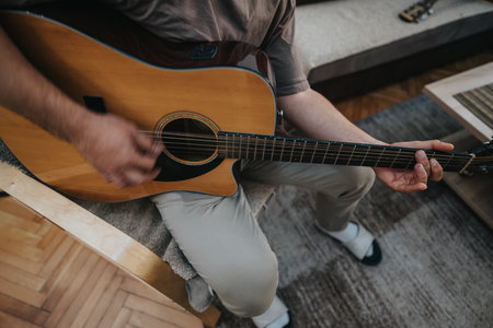 Person plays acoustic guitar indoors, seated on a couch, practicing music at home
