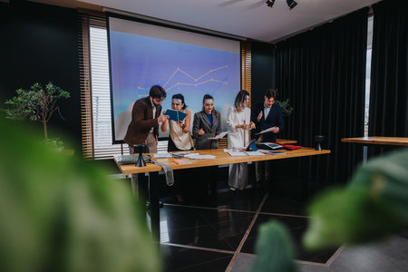 Business meeting: coworkers collaborate around a table presenting charts and reviewing documentsの写真素材