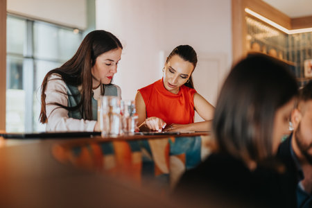 Two colleagues review documents at a cafe bar, sharing ideas and smiles during a casual business meetingの写真素材