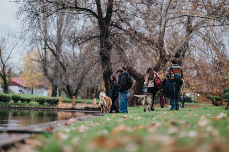 Teenagers with dogs in a park by the water during autumn, casual group moment outdoorsの写真素材