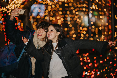 Teenage friends take a joyful selfie beneath festive city lights during a night out
