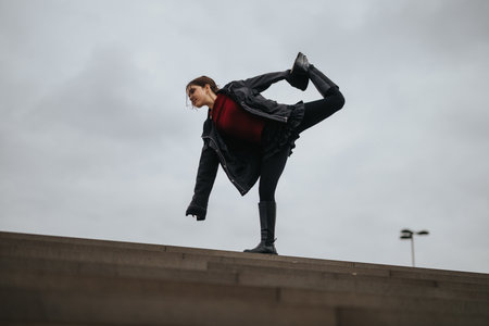 Young woman balances on a concrete ledge in an urban setting, showcasing street style and athletic...