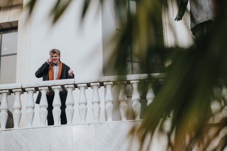 Man on balcony in winter speaks on phone, dressed in scarf and coat, urban business sceneの写真素材