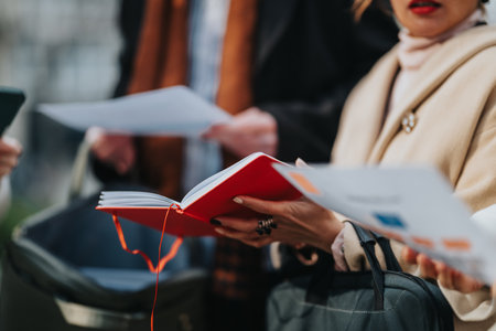 Business people review documents and a red notebook in an outdoor urban setting, a professional sceneの写真素材