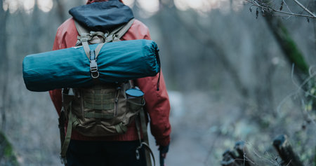 Woman hiker on forest trail with backpack and blue rolled sleeping mat for camping