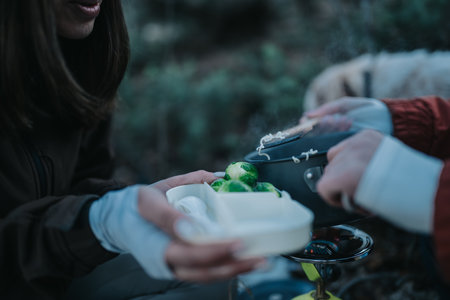 Outdoor camping scene with two women cooking and sharing food over a portable stoveの写真素材